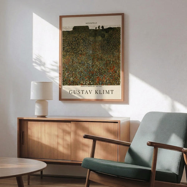 May include: Framed Gustav Klimt poster print showing a colorful wildflower field with green hills and trees in the background, displayed above a wooden mid-century modern credenza with a white ceramic table lamp. A sage green upholstered armchair with wooden arms sits nearby on a wooden floor, with natural sunlight casting geometric shadows across the white wall.