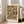 May include: Framed poster leaning against white wall next to beige sofa in bright living room. Artwork shows colorful portrait of woman with long dark hair surrounded by ornate floral and decorative patterns in greens, oranges, and earth tones. Text reads "Portrait of Friederike Maria Beer 1916" and "Gustav Klimt" in black letters on cream background below image.