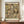 May include: Framed art print featuring Gustav Klimt's colorful portrait of a woman with long flowing hair surrounded by decorative figures and ornate patterns in yellows, greens, and earth tones. The poster displays against a cream wall on a wooden sideboard next to a white ceramic vase and stacked books in a modern interior setting.