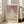 May include: Framed art print leaning against beige couch in bright living room with white walls and wooden floors. Print shows young girl in white dress with floral details against purple patterned background, standing on colorful decorative ground. Text reads "MADA PRIMAVESI 1912" and "GUSTAV KLIMT" in simple black letters on cream background below artwork.