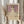 May include: Hands holding framed art print of young girl in white dress with floral details against purple background, displayed in light wood frame. Person wears beige ruffled sleeves, holds dried wheat stems, standing by white curtained window in soft natural lighting.