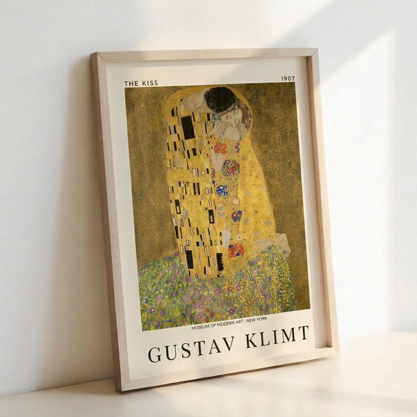 May include: Framed art print of Gustav Klimt's "The Kiss" from 1907, showing two embracing figures in golden robes with geometric patterns against a shimmering gold background. The woman's dress features colorful floral motifs while standing on a flower-filled meadow. Print displayed in light wood frame leaning against white wall, showing Museum of Modern Art attribution at bottom.