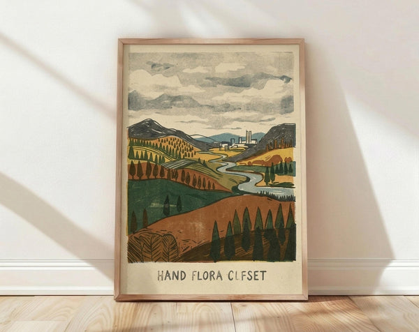May include: Framed vintage-style landscape print leaning against white wall on light wood floor. Artwork shows rolling hills in autumn colors - greens, oranges, and browns - with winding river, scattered evergreen trees, and industrial buildings in distance under cloudy sky. Hand-lettered text below illustration reads "HAND FLORA OFFSET" in simple block letters. Natural wood frame with warm tone complements earthy artwork palette.