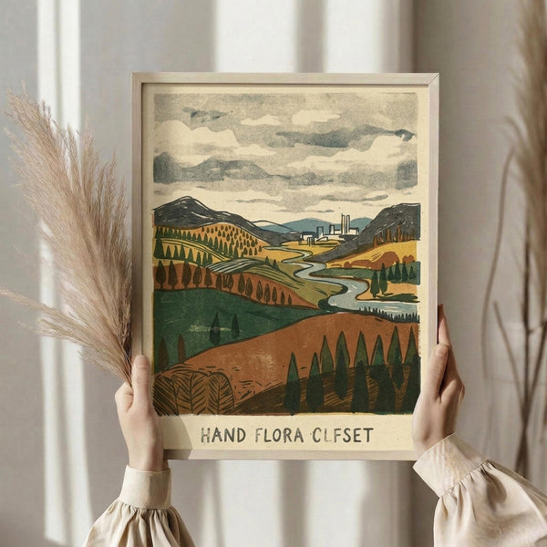 May include: Person in beige ruffled sleeves holding framed landscape print showing rolling hills, winding river, distant industrial buildings, and cloudy sky in muted greens, browns, and yellows. Light wooden frame against white curtained window with dried pampas grass stems visible to the left.