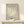 May include: Framed vintage-style art print featuring cream-colored coral or seaweed design on sage green background with "MATISSE PAPIERS DÉCOUPÉS" and "BERGGRUEN & CIE" text, displayed in thin gold frame on light wood console table next to small wrapped white gift with twine and greenery sprig against cream wall