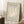 May include: Framed beige and cream Matisse exhibition poster featuring abstract coral-like botanical form, displayed leaning against white wall corner on textured white rug. Light wood frame, soft natural lighting creates geometric shadows. Coffee cup on wooden block visible to left, cozy neutral interior setting.