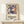 May include: Framed poster featuring abstract dancing figures in purple, blue, orange and yellow cut-out style shapes against cream background, displayed on light wood console table beside small wrapped gift with twine and greenery sprig against white wall