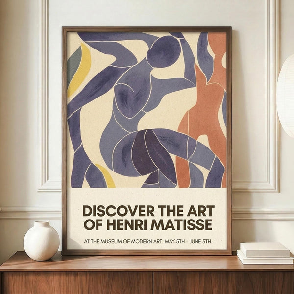 May include: Framed poster featuring abstract cut-out style figures in blue, coral orange, and yellow tones with curved, flowing forms reminiscent of dancers. Exhibition-style text below reads "Discover the Art of Henri Matisse" with museum details. Displayed on wooden sideboard next to white ceramic vase and stacked books in elegant room with cream walls and white molding.