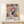 May include: Framed abstract art print in light wood frame featuring colorful geometric shapes in pink, blue, yellow, orange and black with "MATISSE" text at bottom, displayed on white wooden shelf next to small wrapped gift with twine and greenery sprig against cream wall