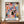 May include: Framed colorful abstract art poster with geometric shapes in pink, blue, orange, yellow and black with "MATISSE" text at bottom, displayed on wooden sideboard next to white ceramic vase and books in elegant room with cream walls and crown molding.
