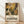 May include: Framed poster with colorful botanical illustration featuring stylized flowers and leaves in yellow, brown, green, and black tones. Exhibition-style text below reads "DISCOVER THE ART OF HENRI MATISSE" with museum and date details. Light wood frame rests against white wall on natural wood flooring with soft shadows cast across the scene.