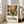 May include: Framed botanical art print with colorful abstract flowers and leaves in yellow, brown, green, and black tones, displayed on light wooden floors against white walls next to a beige sofa. The poster features exhibition text about Henri Matisse and shows layered floral collage elements with various leaf patterns and blooms in an earthy, vintage-inspired color palette.