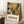 May include: Framed poster with botanical illustration featuring yellow and brown flowers, green and black leaves, and ferns in Matisse's cut-out style. White text below reads "Discover the Art of Henri Matisse" with museum exhibition details. Poster leans against white wall on textured rug next to wooden side table with white coffee cup and saucer.