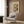 May include: Cream-colored Henri Matisse poster with abstract floral design in orange, yellow, green and blue tones, displayed in light wood frame on textured wood wall panel. Modern beige armchair with geometric patterned pillow sits below artwork. Gold floor lamp and dark side table with open book complete the warm, contemporary interior scene.