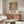 May include: Colorful abstract art poster featuring vibrant fruits, flowers and foliage in yellows, oranges, greens and blues, displayed in thin wooden frame above walnut credenza in modern living room with cream chair, glass coffee table and minimalist decor