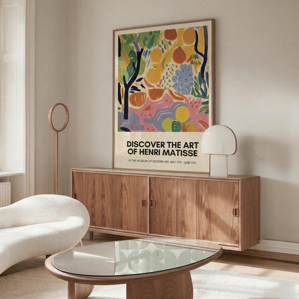 May include: Colorful abstract art poster featuring vibrant fruits, flowers and foliage in yellows, oranges, greens and blues, displayed in thin wooden frame above walnut credenza in modern living room with cream chair, glass coffee table and minimalist decor