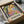 May include: Colorful Henri Matisse-style art print featuring abstract fruits, flowers and foliage in vibrant yellows, greens, blues, pinks and oranges, displayed in black frame inside cardboard shipping box with protective tissue paper wrapping on white surface