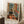 May include: Framed Henri Matisse art print showing colorful interior scene with black and white cat on orange wooden floor, green chair, bed, and French doors opening to bright rooms beyond. Print features vibrant blues, oranges, and greens in Matisse's distinctive style. Frame leans against white wall next to coffee cup on wooden block and textured throw blanket in cozy room setting.