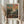 May include: Hands holding a framed art print featuring an impressionist landscape painting with vibrant brushstrokes in blues, oranges, pinks, and greens depicting trees and figures beneath a colorful sky. The print has "Henri Matisse Paris" text below the artwork in a light wooden frame. Dried pampas grass and neutral curtains create a soft, natural backdrop.
