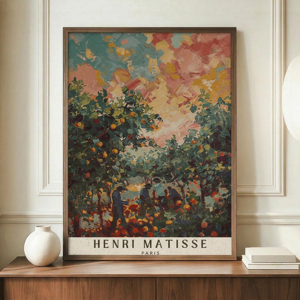 May include: Framed art print featuring a colorful landscape painting with vibrant orange and pink sky, green foliage and fruit trees in foreground, displayed on wooden sideboard next to white ceramic vase and books in elegant room with cream walls and white molding.