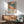 May include: Framed Matisse exhibition poster showing vibrant tropical landscape with palm trees in blues, greens, oranges and pinks, displayed above wooden sideboard with white ceramic lamp in modern living room setting with mint green mid-century armchair and natural lighting creating wall shadows.