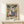May include: Vintage-style poster print of Mediterranean coastal scene with palm trees, white sailboats on blue water, terracotta buildings, and decorative balcony with potted plants. Text reads "MATISSE" at bottom. Displayed in thin gold frame on light wood surface with small wrapped gift box beside it against cream wall.