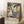 May include: Framed vintage-style travel poster featuring tropical coastal scene with palm trees, sailboats on blue water, Mediterranean buildings, and "MATISSE" text at bottom. Poster leans against white wall next to coffee cup on wooden surface and beige textured throw blanket in corner of bright room.