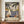 May include: Framed vintage-style travel poster featuring sailboats on blue water surrounded by palm trees, with "MATISSE" text at bottom. Poster displayed on wooden sideboard next to white ceramic vase and stacked books in room with white walls and crown molding. Warm Mediterranean coastal scene with terra cotta buildings and mountains in background.