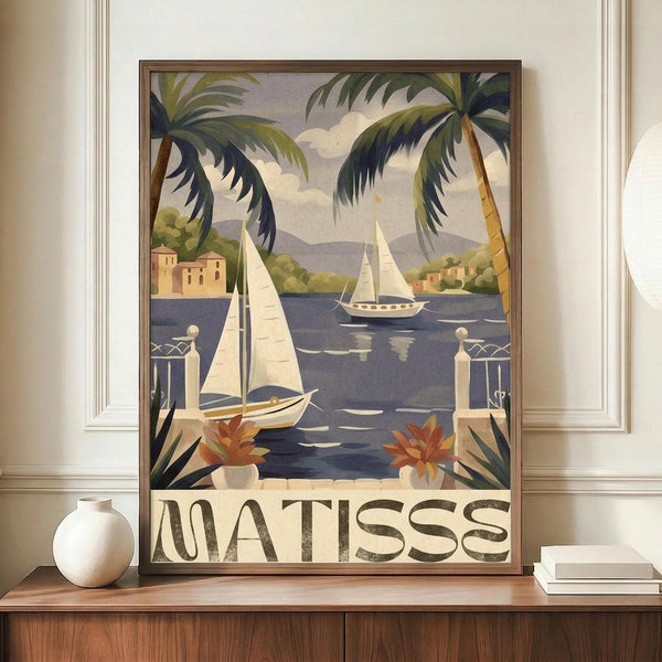 May include: Framed vintage-style travel poster featuring sailboats on blue water surrounded by palm trees, with "MATISSE" text at bottom. Poster displayed on wooden sideboard next to white ceramic vase and stacked books in room with white walls and crown molding. Warm Mediterranean coastal scene with terra cotta buildings and mountains in background.