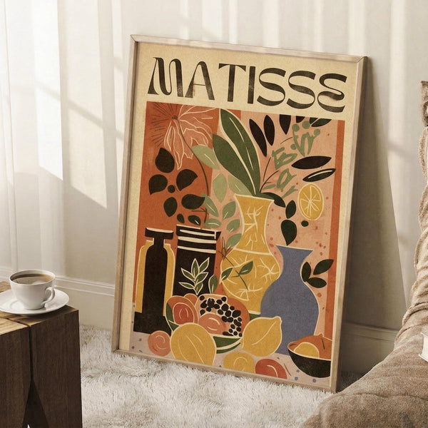 May include: Framed art print in light wood frame leaning against white wall corner. Poster features colorful still life with botanical elements, vases, bottles, and fruits in earthy tones of orange, yellow, green, and blue. Scene includes coffee cup on wooden block and textured beige throw blanket, creating cozy room setting with natural lighting.