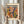 May include: Person in beige ruffled sleeves holding framed Matisse exhibition poster with abstract colorful cut-out shapes in blues, oranges, yellows, and greens. Dried pampas grass stems visible on left side. Light wooden frame against neutral curtained background in soft natural lighting.
