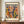 May include: Framed Matisse exhibition poster featuring abstract cut-out style artwork in vibrant colors including purple, orange, yellow, green, and pink geometric shapes and circles on cream background. Dark wooden frame displayed on walnut credenza beside white ceramic vase and stacked books against beige wall with white trim molding.
