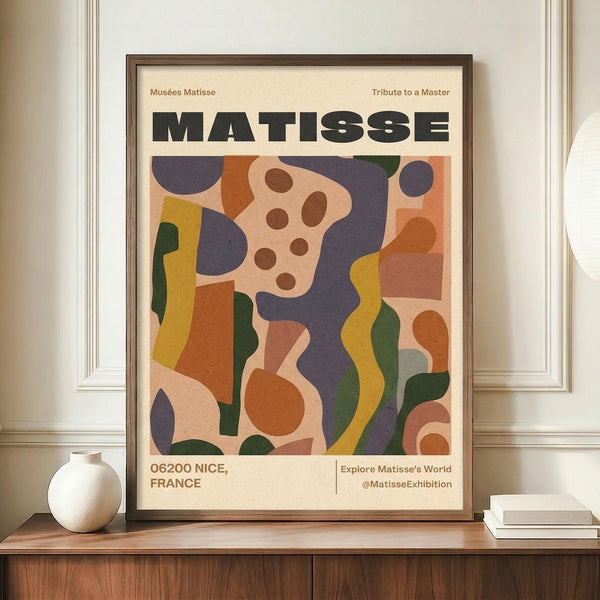 May include: Framed Matisse exhibition poster featuring abstract cut-out style artwork in vibrant colors including purple, orange, yellow, green, and pink geometric shapes and circles on cream background. Dark wooden frame displayed on walnut credenza beside white ceramic vase and stacked books against beige wall with white trim molding.