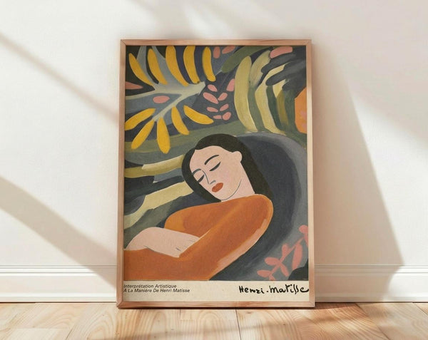 May include: Framed art print leaning against white wall on wooden floor with natural light shadows. Shows woman with closed eyes, long dark hair, wearing orange top, surrounded by tropical foliage in yellow, green, and coral tones. Fauvist style with bold, flat colors and organic shapes. Light wood frame, poster appears medium-sized against room setting.