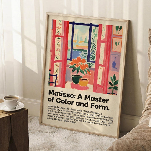 May include: Framed art poster featuring a colorful Matisse-style interior scene with red open window shutters, orange flowers in vases, and view of sailboats on water. Exhibition text reads "Matisse: A Master of Color and Form" below the artwork. Poster leans against white wall next to white coffee cup on wooden surface and beige textured throw blanket in bright, airy room setting.