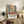 May include: Framed Henri Matisse exhibition poster featuring colorful collage artwork with geometric patterns, botanical motifs, and warm tones of orange, green, and blue. The poster sits on a rustic wooden sideboard alongside books, a ceramic vase, and fern plant, with cream upholstered furniture visible in a neutral-toned living room setting.