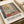 May include: Vintage-style art exhibition poster featuring a colorful window scene with green foliage and geometric patterns in warm earth tones, displayed on white paper with a beige ribbon nearby on a cream-colored surface