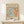 May include: Framed Matisse exhibition poster with abstract coral and teal leaf patterns on cream background, displayed on light wood console table next to small white gift box with greenery, against neutral wall with soft natural lighting.