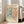 May include: Framed vintage-style exhibition poster featuring abstract coral and teal organic shapes in Matisse's cut-out style, displayed on wooden floor beside beige sofa in bright living room with large windows. Cream-colored frame complements the warm neutral interior.