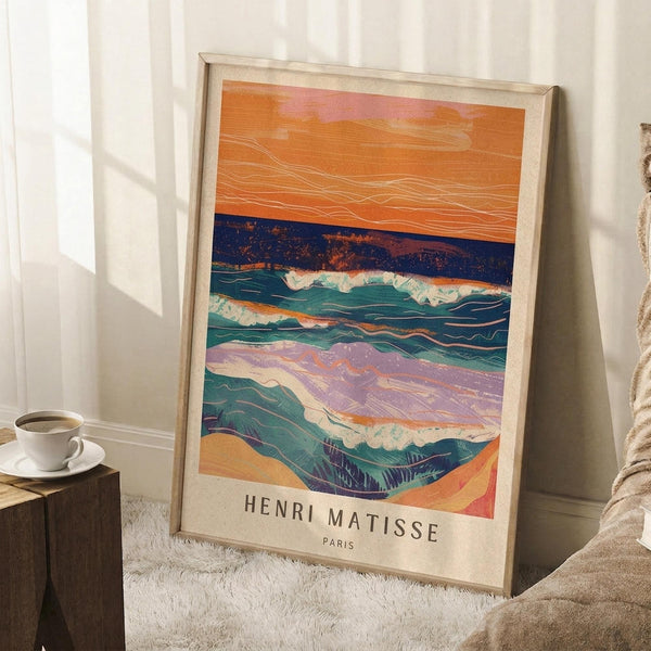 May include: Framed vintage-style poster featuring abstract seascape with layered waves in teal, orange, purple and blue tones against orange sky, displayed leaning against white wall corner next to wooden side table with coffee cup, positioned on textured white rug beside beige blanket in bright natural lighting