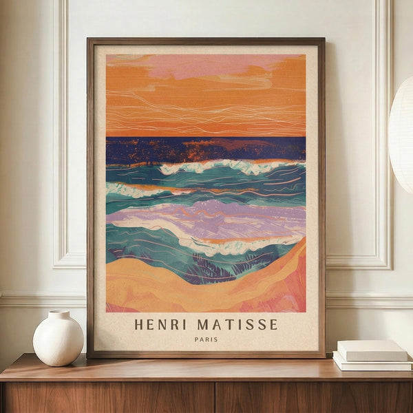 May include: Framed art print displaying an abstract coastal landscape with flowing waves in teal and purple, golden sandy beach, and warm orange-pink sunset sky with flowing linear details. The print features "HENRI MATISSE PARIS" text at bottom. Shown in thin dark wooden frame on walnut credenza beside white ceramic vase and stacked books in neutral-toned room with white paneled walls.