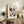 May include: Framed Henri Matisse-inspired portrait poster displayed on rustic wooden console table. Abstract face features red and blue color blocking around eyes, red lips, black hair against cream background. Light wood frame, surrounded by fern plant, leather chair, ceramic vases and books in neutral-toned living room setting.
