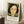 May include: Framed portrait poster in light wood frame leaning against white wall on textured white rug. Artwork shows woman with dark bob haircut, pale complexion, and colorful floral background in greens and oranges. Poster has white border with Henri Matisse text and quote below image. Coffee cup on wooden block visible to left, beige throw blanket on right side of scene.