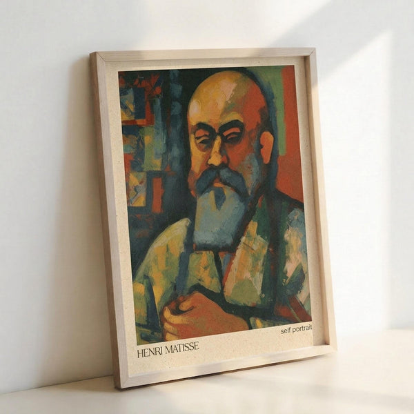 A framed art print leaning against a white wall showing a colorful expressionist self-portrait of a bald man with a mustache and beard. The painting features bold brushstrokes in warm oranges, yellows, greens, and blues with the subject wearing what appears to be a jacket. The artwork is displayed in a light wooden frame with white matting, and "HENRI MATISSE" and "self portrait" text appears at the bottom of the print.