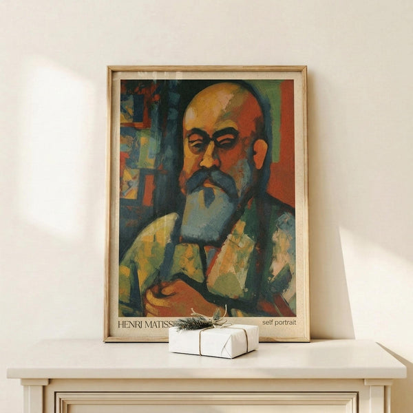 May include: Framed art print of a bearded man's portrait in vibrant colors including orange, green, and blue brushstrokes, displayed on a white wooden shelf next to a small wrapped gift box with twine and greenery sprig against a cream wall.