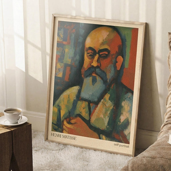 May include: A framed art print featuring a colorful portrait of a bearded man in Fauve style with bold oranges, greens, and blues, displayed on a white fluffy rug against white walls with natural window light, alongside a coffee cup on a wooden surface and cream-colored fabric.