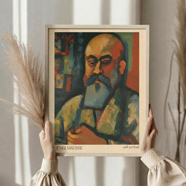 May include: Hands holding a framed art print of a colorful expressionist self-portrait showing a bearded man with glasses in warm oranges, greens, and blues. The wooden frame sits against white curtains with dried wheat stems visible on the left side.