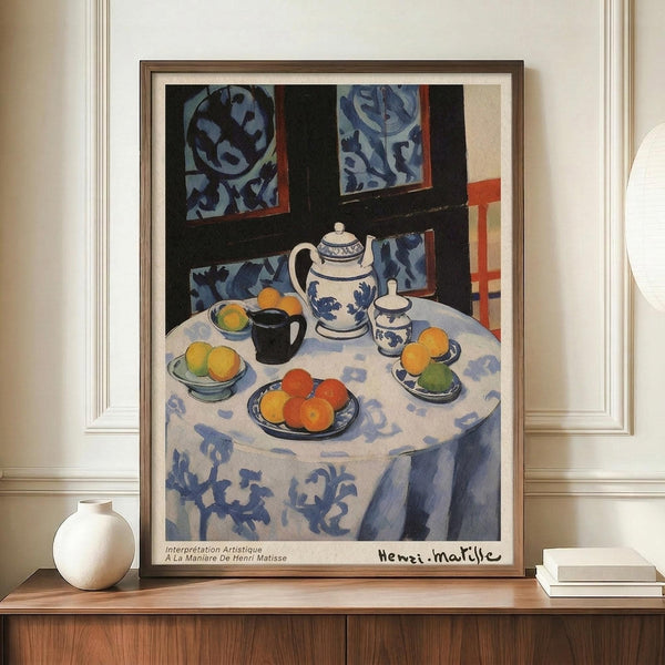 May include: Framed poster print featuring a colorful still life painting in Matisse's style, showing a round table with white patterned tablecloth, blue and white teapot, fruit bowls with oranges and lemons, coffee cup, and decorative blue patterned wallpaper background. Print displayed on wooden console table with small white ceramic vase and books in modern room setting with white walls and molding.