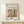 May include: Framed art poster featuring Matisse-inspired still life with plants, vases, and fruits in earthy tones of green, terracotta, and cream. Text reads "Discover the Beauty of Matisse's Art" above colorful botanical illustration. Natural wood frame displayed on light wooden surface with small wrapped gift box beside it against cream wall with soft shadows.
