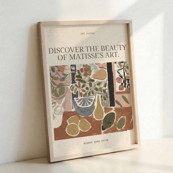 May include: Framed art poster featuring a colorful still life illustration in Matisse's style, showing potted plants, fruits, and decorative objects in earthy tones of green, brown, and coral. The poster has cream background with black text reading "DISCOVER THE BEAUTY OF MATISSE'S ART" and is displayed in a light wood frame leaning against a white wall.
